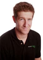 A man with short brown hair wearing a black collared shirt is smiling slightly and looking at the camera against a plain white background, representing Elite Poker Coaching from DeucesCracked. - Poker Training Videos and Poker Coaching A man with short brown hair wearing a black collared shirt is smiling slightly and looking at the camera against a plain white background, representing Elite Poker Coaching from DeucesCracked.